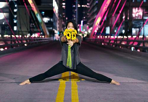 dance pose woman holding sunflowers while splitting at the center of road during nighttime leisure activities